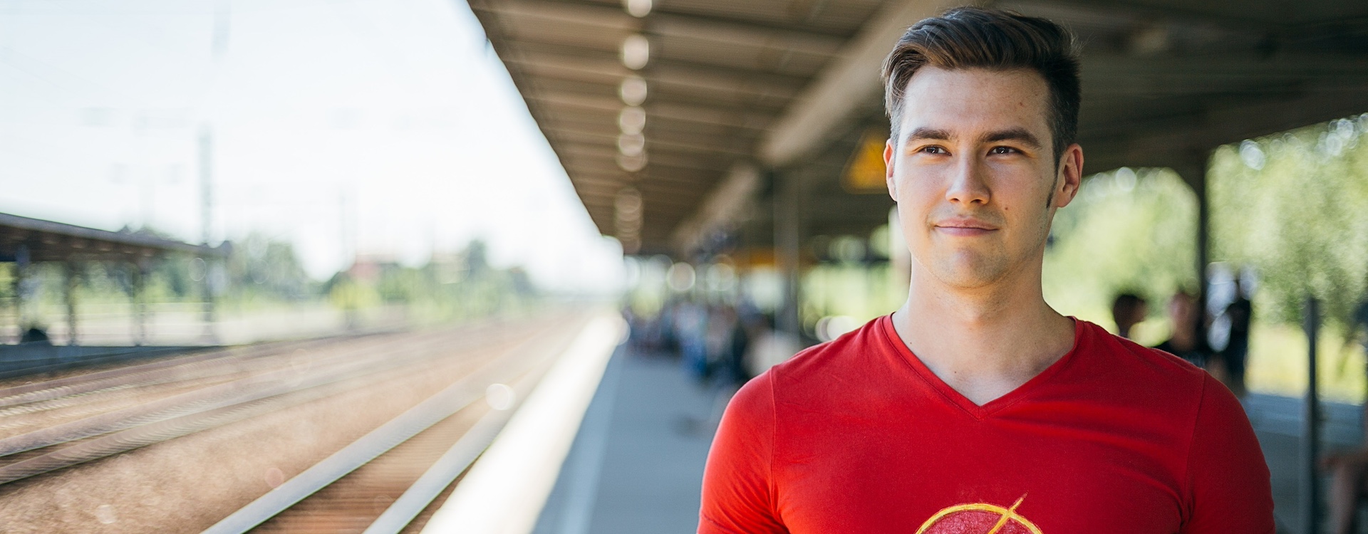 Junger Mann mit rotem Blitzsymbol-T-Shirt steht auf dem Bahnsteig und wartet auf den Zug nach Berlin